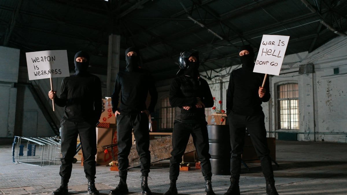 Four masked protesters stand indoors with anti-war signs, advocating peace.