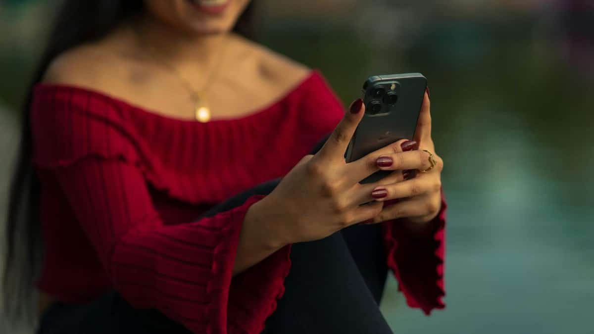 Smiling woman in red sweater using a smartphone outdoors in Mexico City. Captures joyful communication and connection.