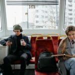 Two commuters on a tram, using gadgets and reading, showcasing a typical urban lifestyle.