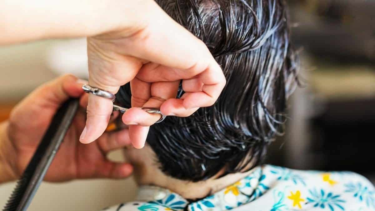 Close-up of a hairstylist cutting short wet dark hair at a salon.