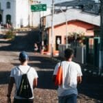Two men walk on a sunny day in a charming town street with colorful houses.