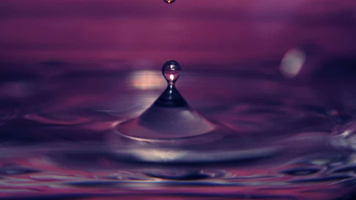 Captivating close-up of a water droplet creating ripples against a vivid purple backdrop.