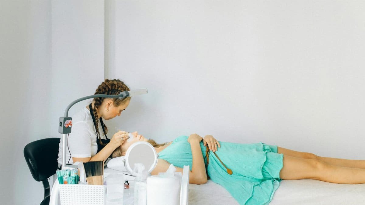 A beautician performing an eyebrow treatment on a client in a modern salon setting.