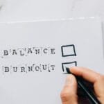 Close-up of a hand hovering over a checklist with options for balance or burnout, symbolizing stress and choice.