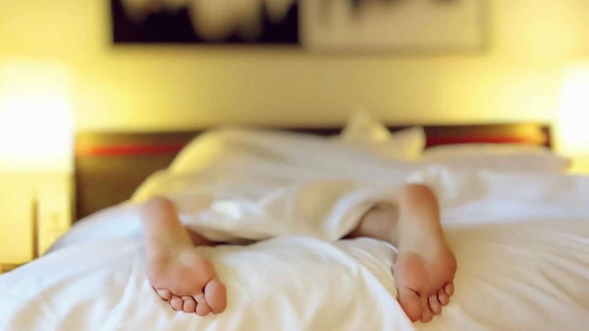 A person relaxing on a bed with feet under white sheets, conveying serenity.