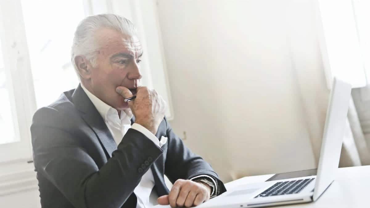 Senior businessman thinking while using a laptop in a bright modern office.