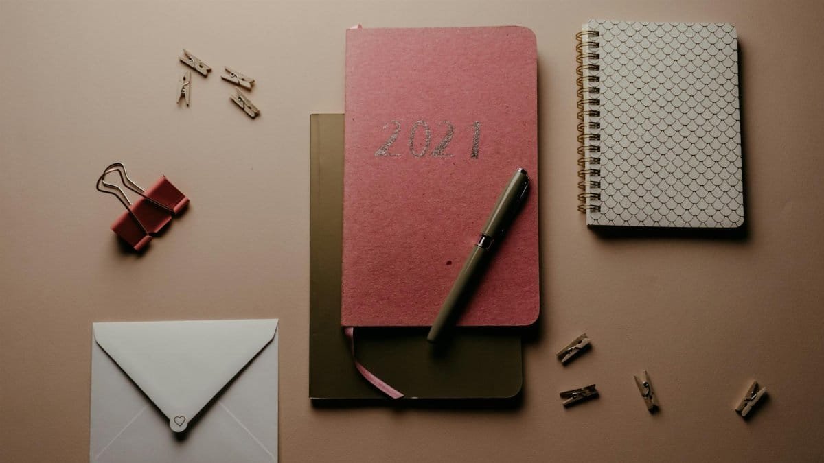 A flat lay image featuring a 2021 planner, notebooks, pen, and stationery with a brown background.