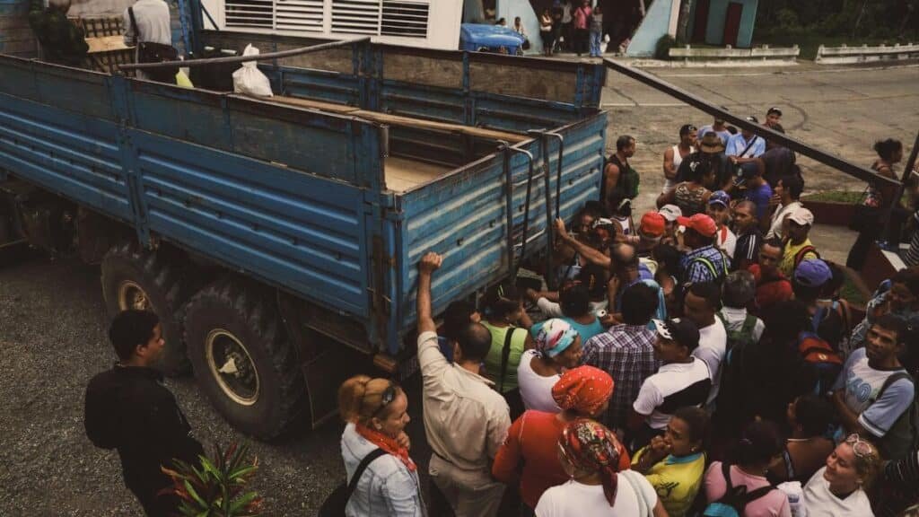 A diverse group of people boarding a blue truck in a rural area, illustrating travel and community.