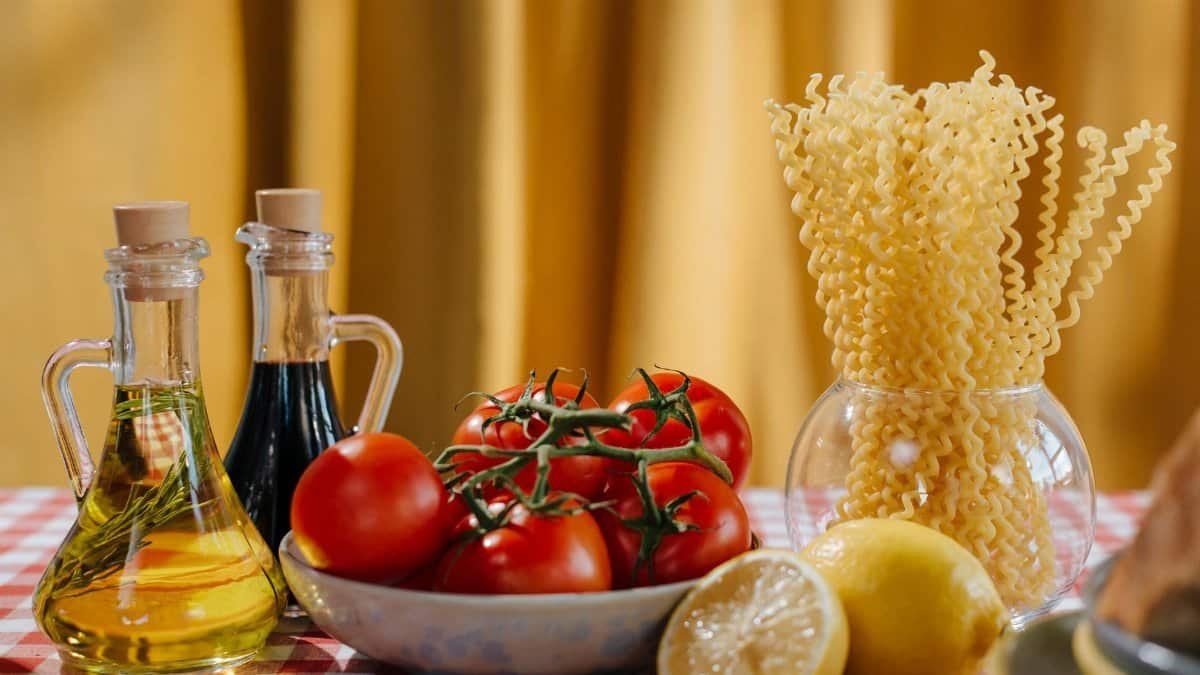 Vibrant still life of Italian cooking ingredients including tomatoes, pasta, and olive oil on a checkered tablecloth.