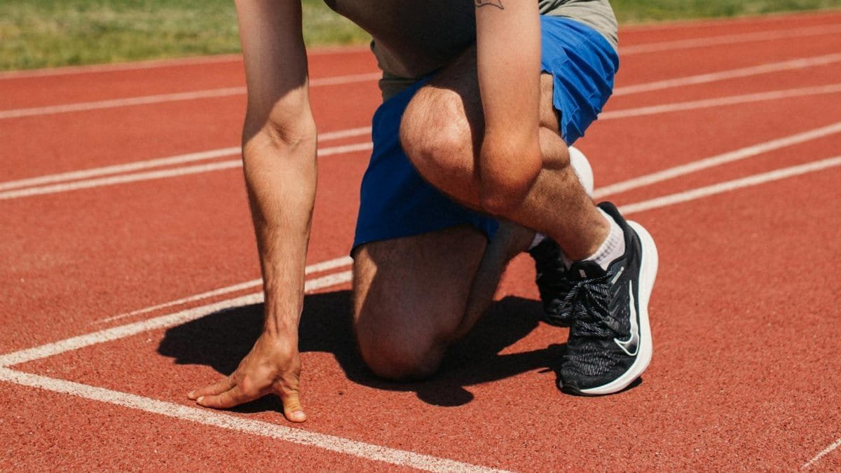Determined athlete at starting line of outdoor track, ready to race with focus and strength.