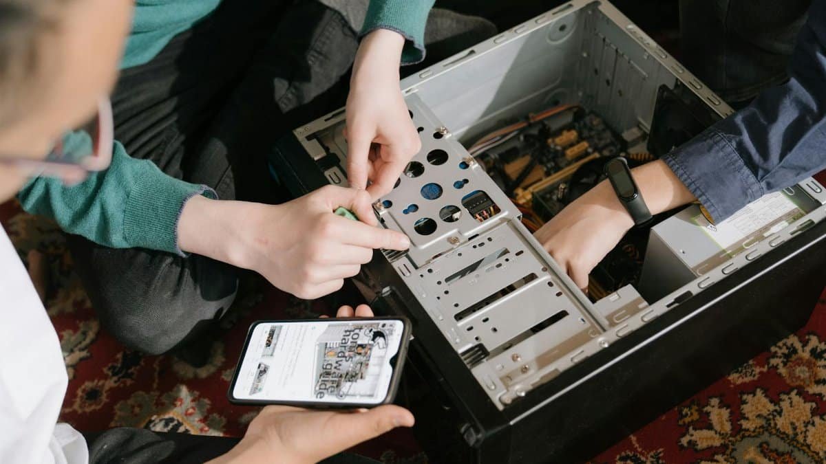 A close-up of hands fixing a computer with guidance from a mobile device.