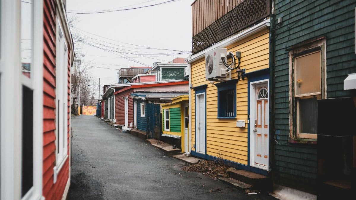 Asphalt way between colorful shabby houses with doors located on street in district of town with power lines against cloudless sky