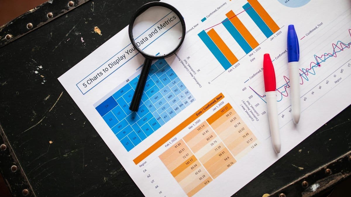 Flat lay of business charts and graphs with magnifying glass and markers on a dark surface.