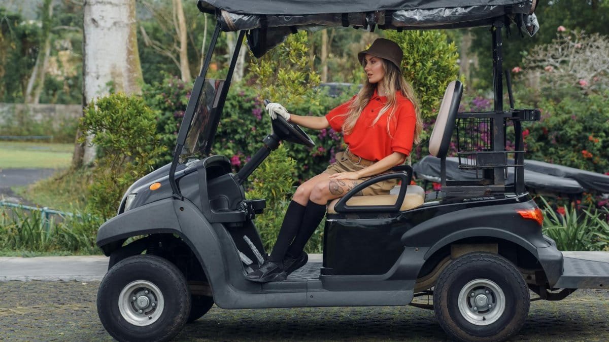 Woman in a golf cart enjoying leisure time outdoors wearing a sun hat and knee socks.