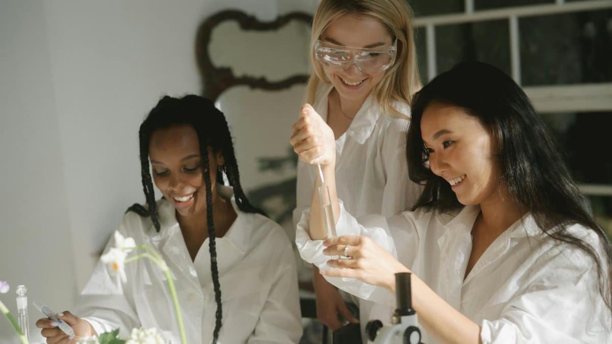 Three women engaging in a science experiment with lab equipment and test tubes.