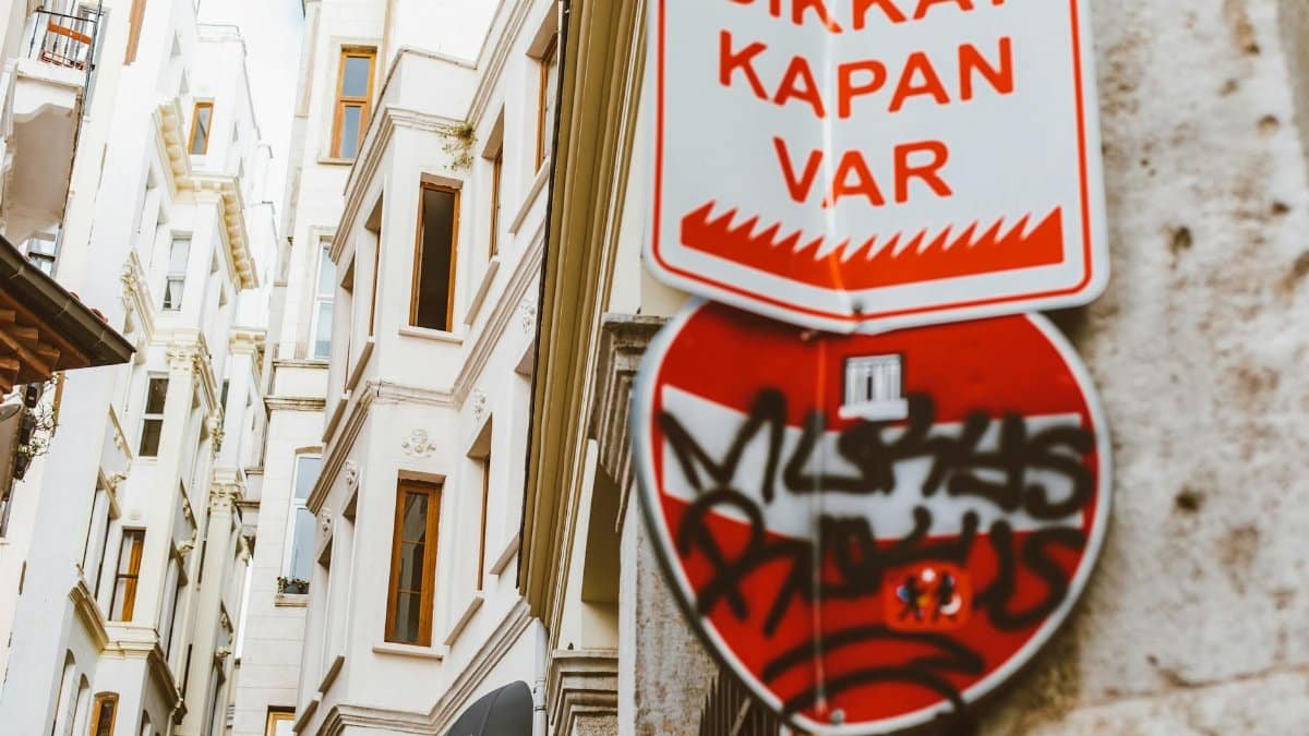 Urban scene featuring Turkish warning sign with graffiti against historic building facades.