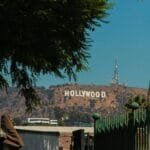 A classic view of the Hollywood sign from a street in Los Angeles, surrounded by urban structures and greenery.