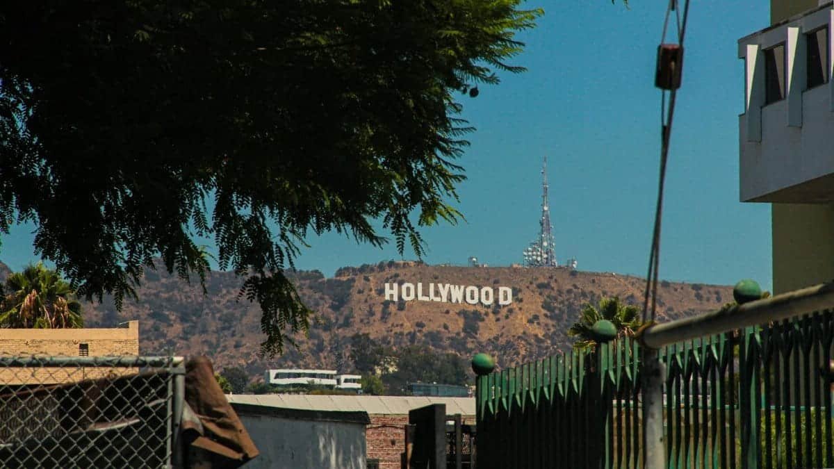 A classic view of the Hollywood sign from a street in Los Angeles, surrounded by urban structures and greenery.