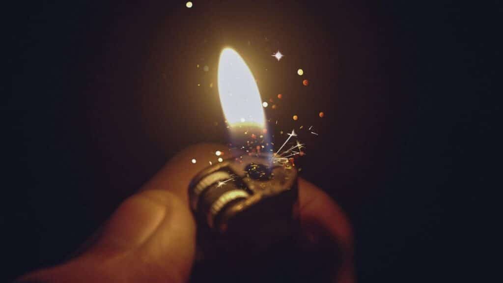 Intense close-up of a lighter igniting a bright flame with spark effects against a dark background.