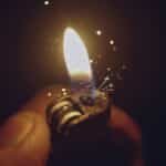 Intense close-up of a lighter igniting a bright flame with spark effects against a dark background.