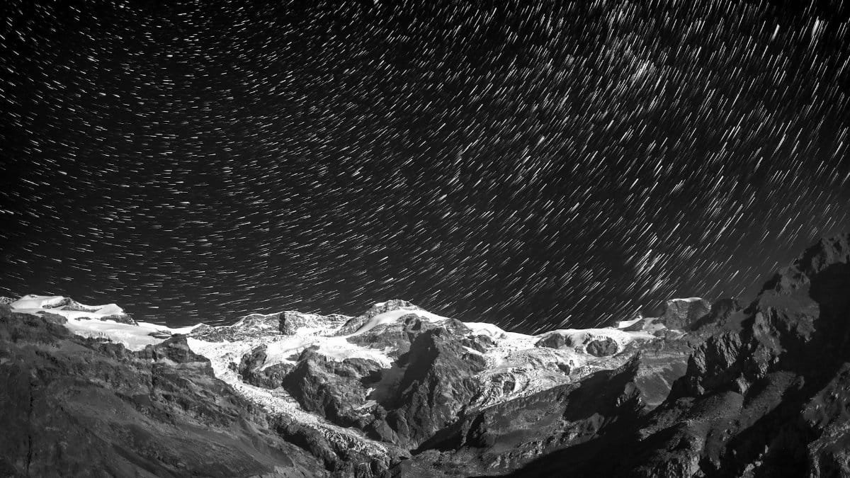 Long exposure of star trails over majestic snow-covered mountains at night.