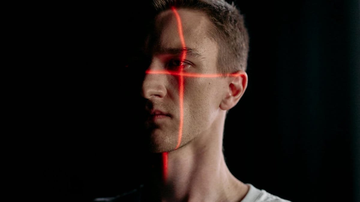 Studio portrait of a man with a laser grid pattern for facial recognition on a black background.