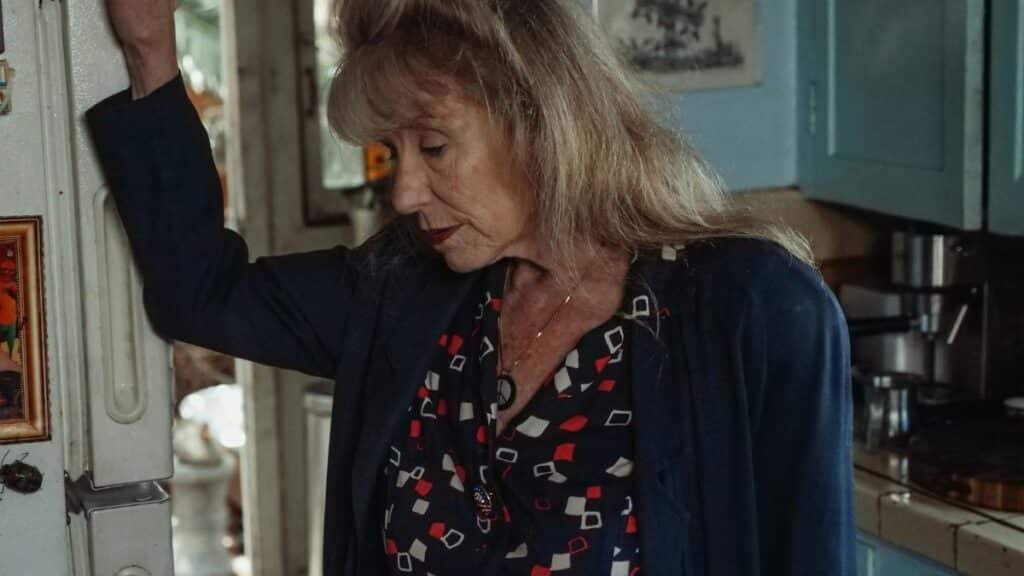 A thoughtful senior woman leans on a refrigerator, evoking emotion and nostalgia in a cozy kitchen setting.