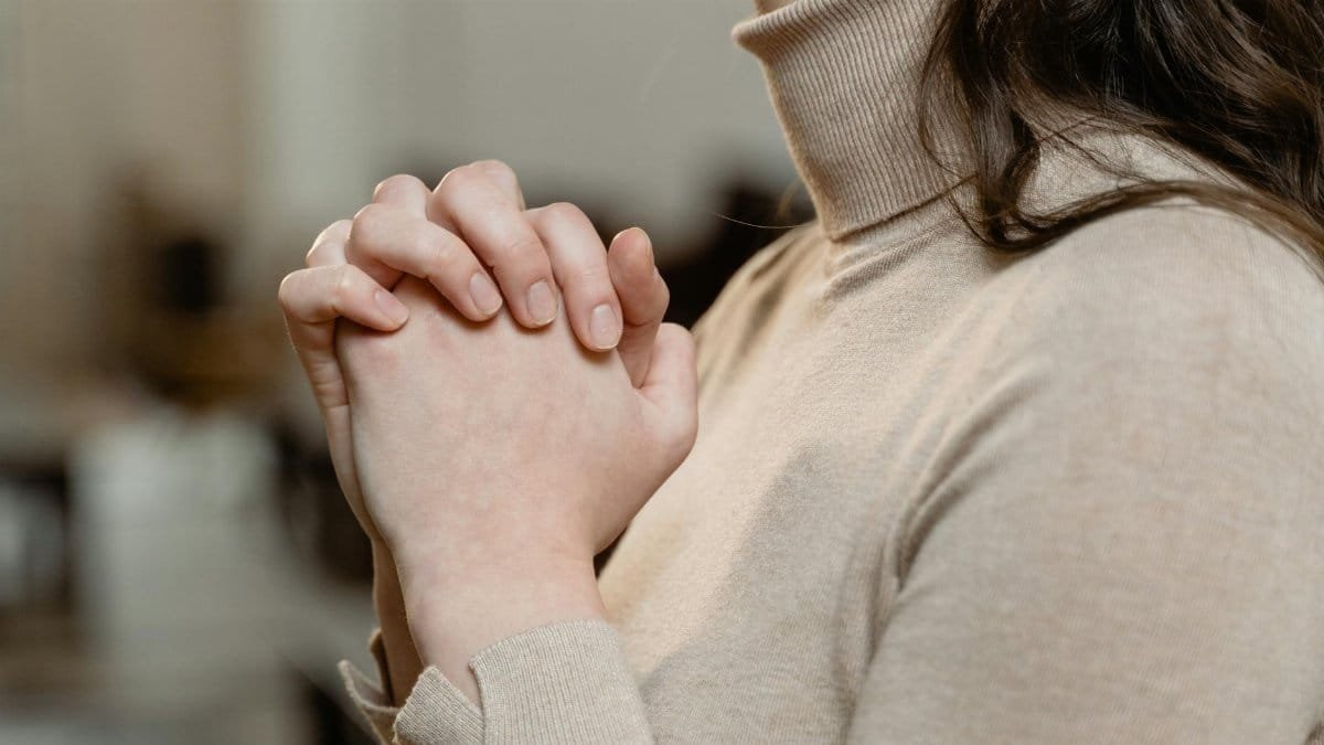 A woman in a turtleneck prays with clasped hands, symbolizing faith and spirituality.