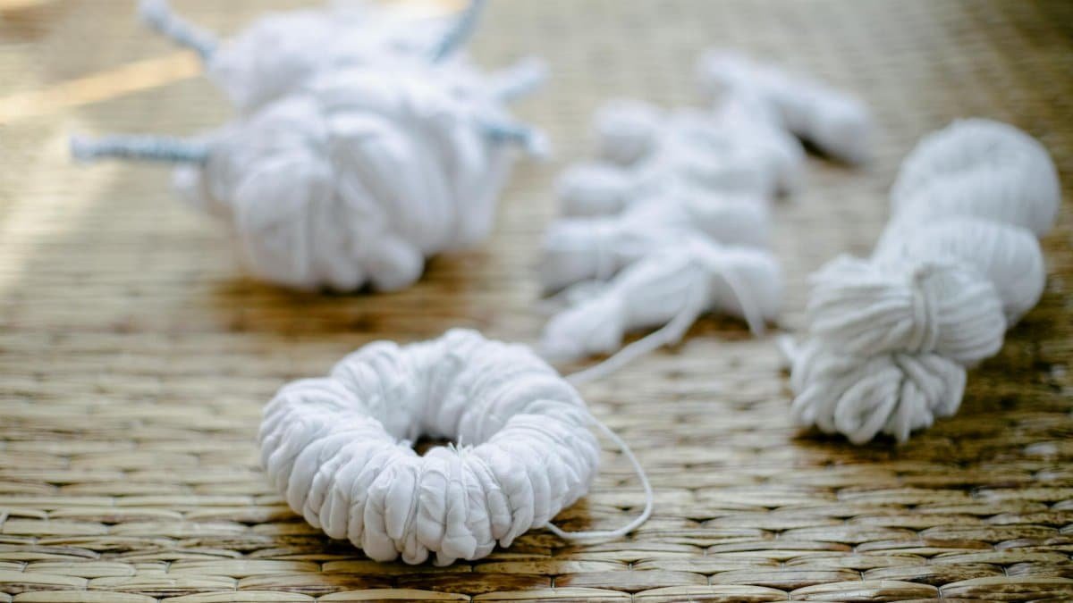 White fabric tied for a traditional shibori dyeing process on a woven mat in sunlight.