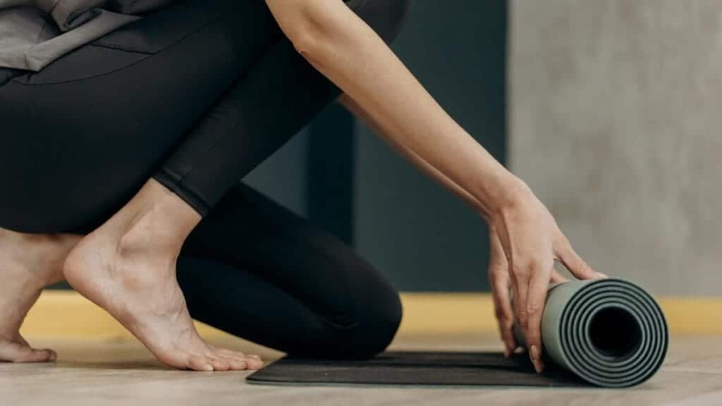 A woman rolling out a yoga mat for an indoor fitness routine, emphasizing calmness and focus.