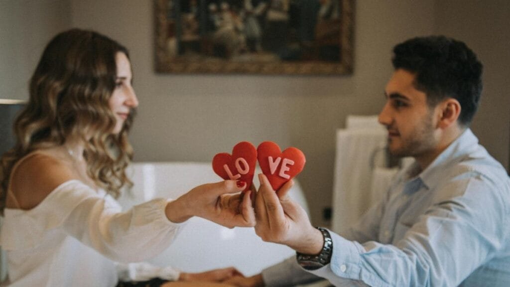 A couple sharing a romantic moment indoors, holding heart-shaped love symbols, enhancing a Valentine's Day feel.