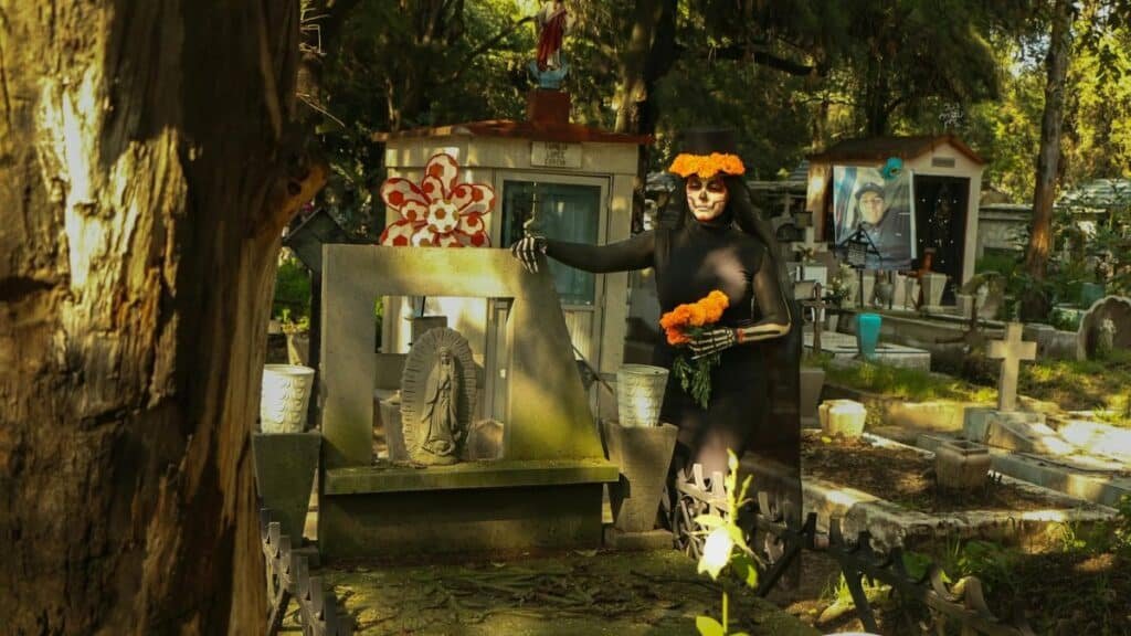 Woman dressed for Día de los Muertos in a cemetery, adorned with marigolds.