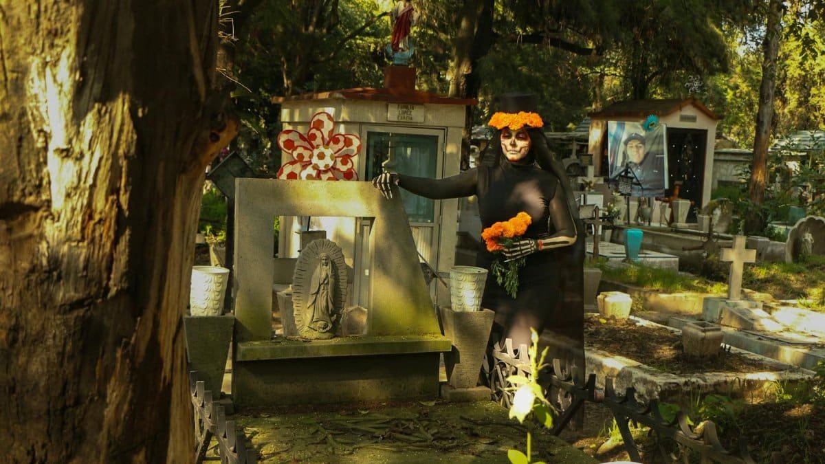 Woman dressed for Día de los Muertos in a cemetery, adorned with marigolds.