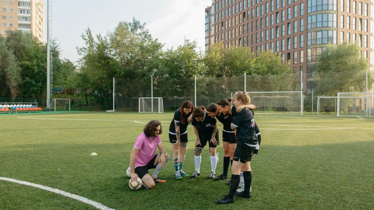 Women's soccer team in a huddle with coach on a sunny day, grass field.
