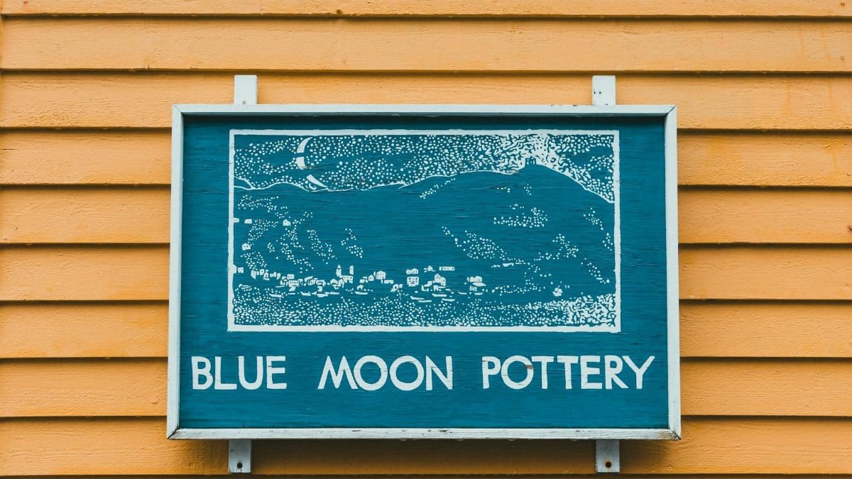 A vivid sign for Blue Moon Pottery displayed on a mustard yellow wooden wall.