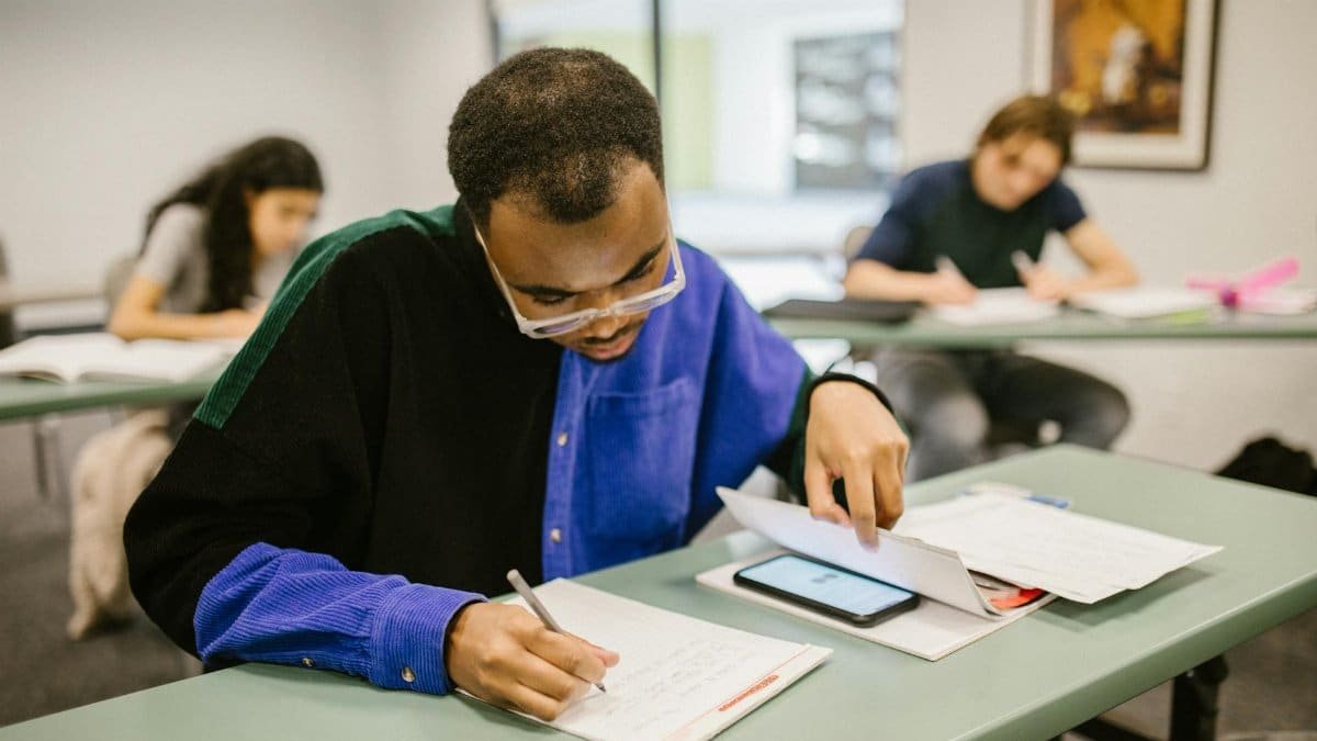 Students taking a test in a classroom setting, focusing on a man writing while others work.