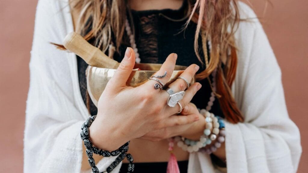 A woman holds a singing bowl with crystals, featuring jewelry and a white shawl, suggesting tranquility and meditation.