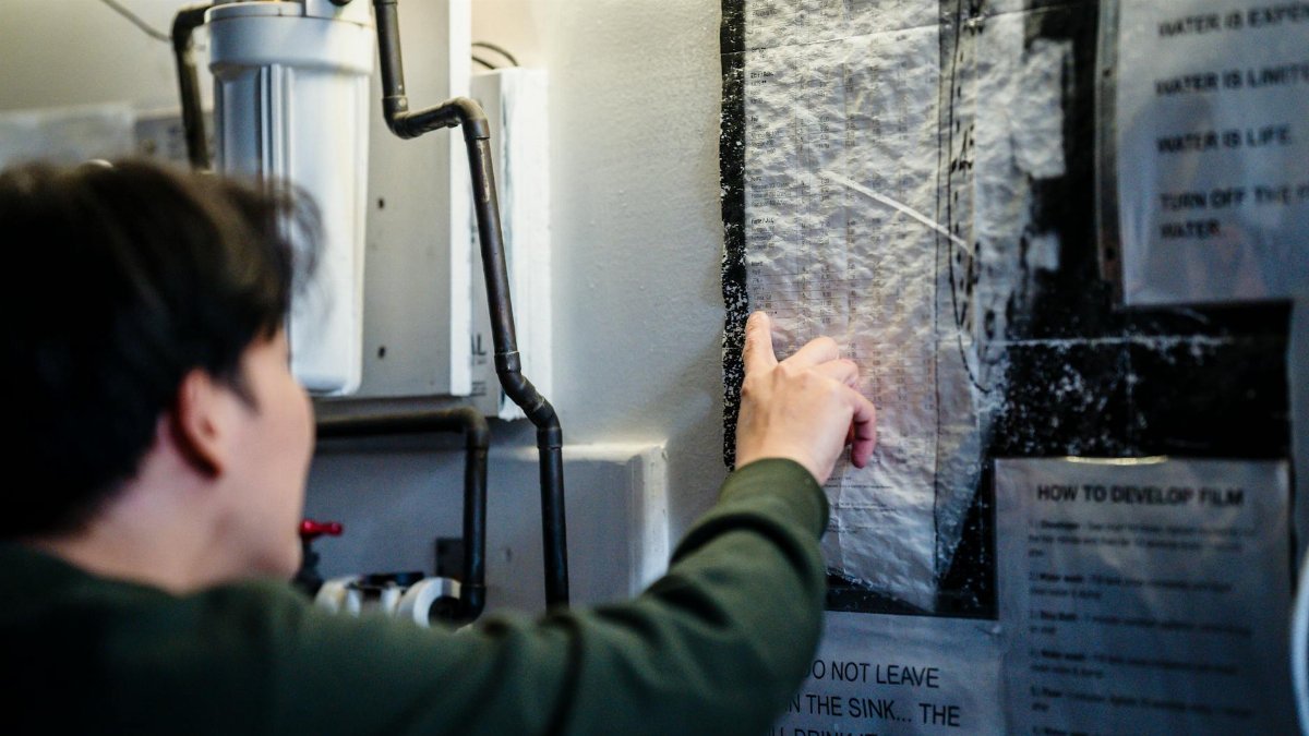 A man pointing at a film development guide on a wall in a workshop setting.