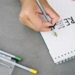 Close-up of hand lettering 'Recycle' on a notepad using drawing materials, emphasizing eco-friendly practices.