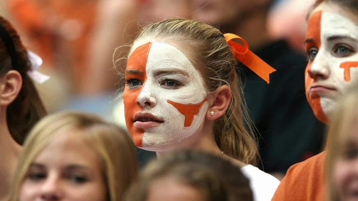 Group of enthusiastic young women with face paint cheering at a sports event.