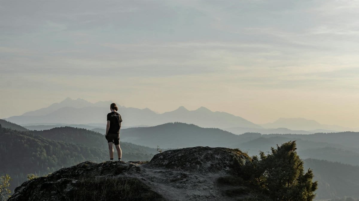 A lone hiker stands on a rock, gazing at a vast misty mountain range at sunrise, capturing a moment of tranquility and adventure.