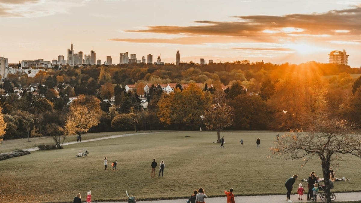Stunning view of Frankfurt skyline at sunset from Lohr Park. Families enjoy the grassy park amidst fall colors.
