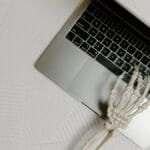 Skeleton hand on laptop keyboard overlaid on papers, symbolizing burnout.