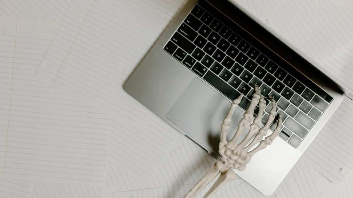 Skeleton hand on laptop keyboard overlaid on papers, symbolizing burnout.
