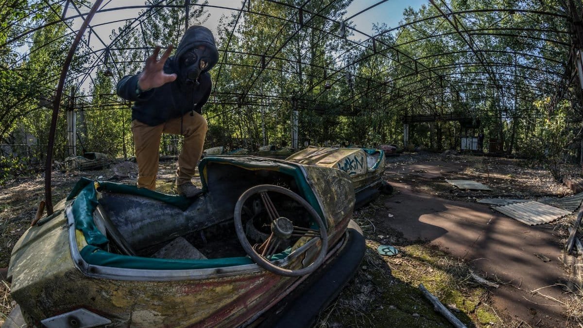 Man in gas mask exploring abandoned bumper cars in Chernobyl theme park.