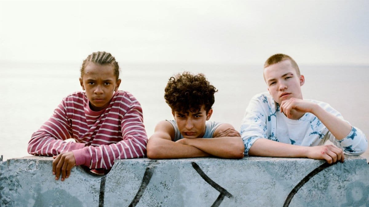 A diverse group of teenagers relaxing by a graffitied wall overlooking the ocean.