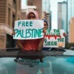 Two individuals holding 'Free Palestine' signs during a peaceful protest in a city center.
