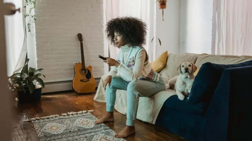 Young woman enjoys a cozy afternoon at home with her dog, watching TV and relaxing.