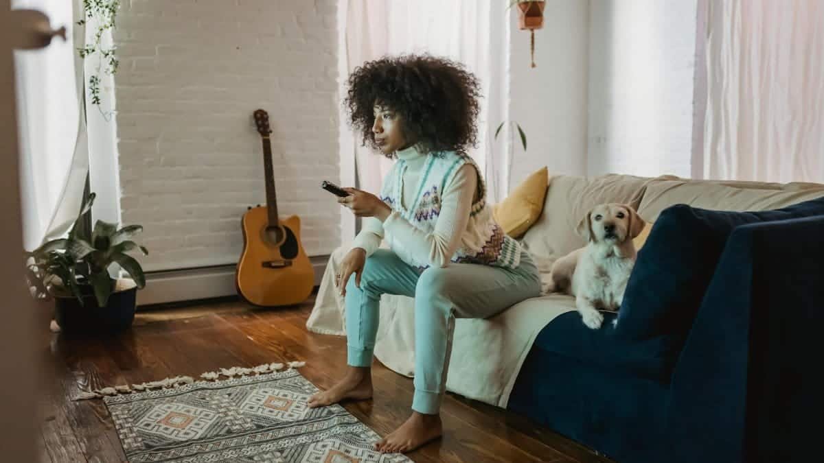 Young woman enjoys a cozy afternoon at home with her dog, watching TV and relaxing.
