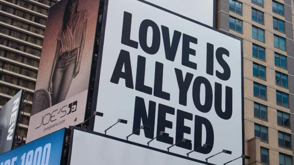 Large city billboard reads 'Love Is All You Need' in New York City street.